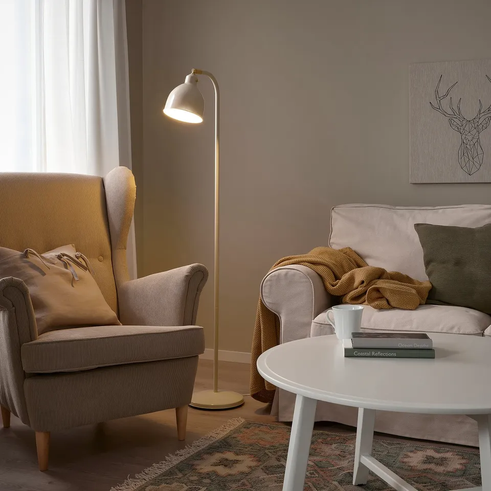 Cosy living space with dainty beige RÖDFLIK lamp between grey armchair and sofa, illuminating a warm, inviting mood.