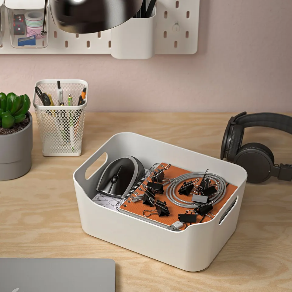 Wooden desk with organised items: white box storing office supplies, headphones, succulent, and pen holder.