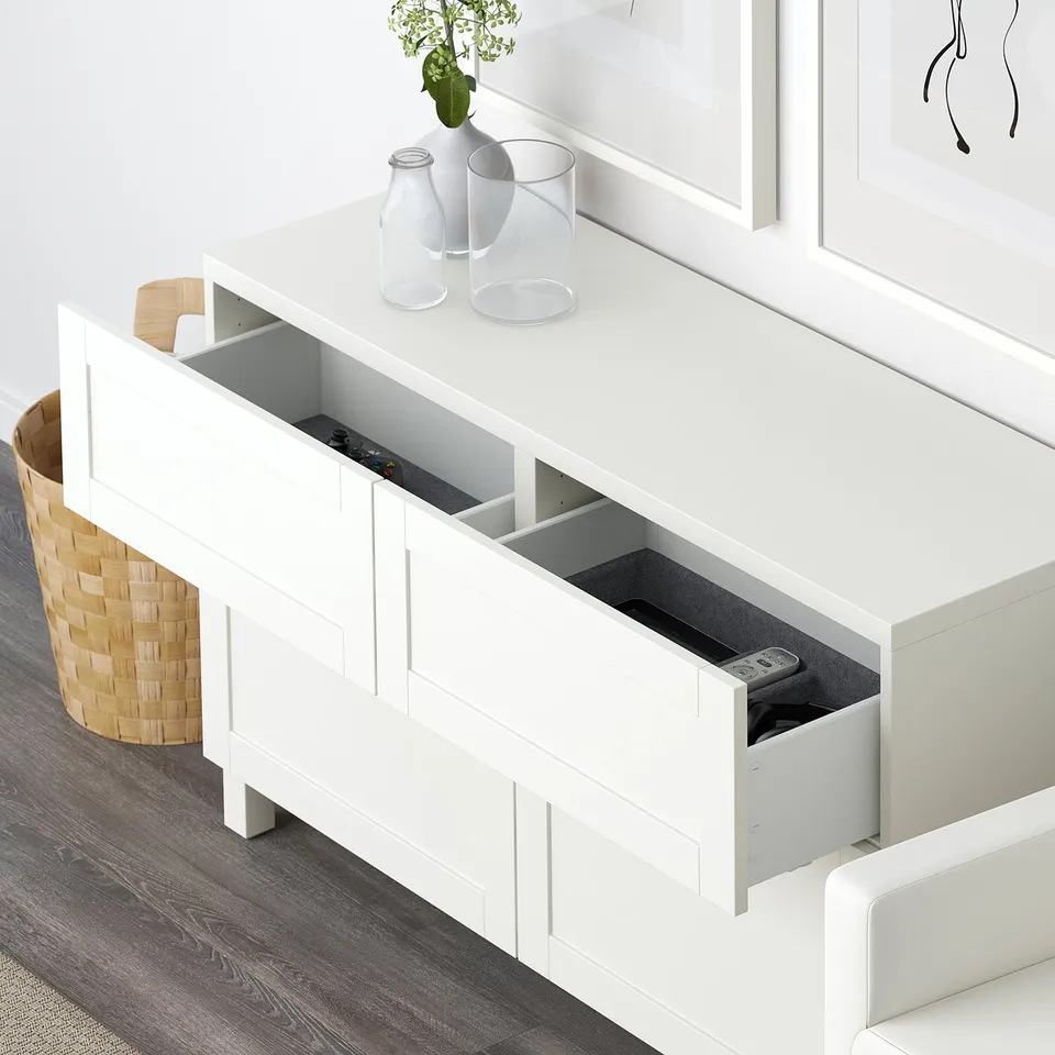 White BESTÅ sideboard with open drawers showing storage space and remote controls inside, hinting at hidden, accessible organisation.