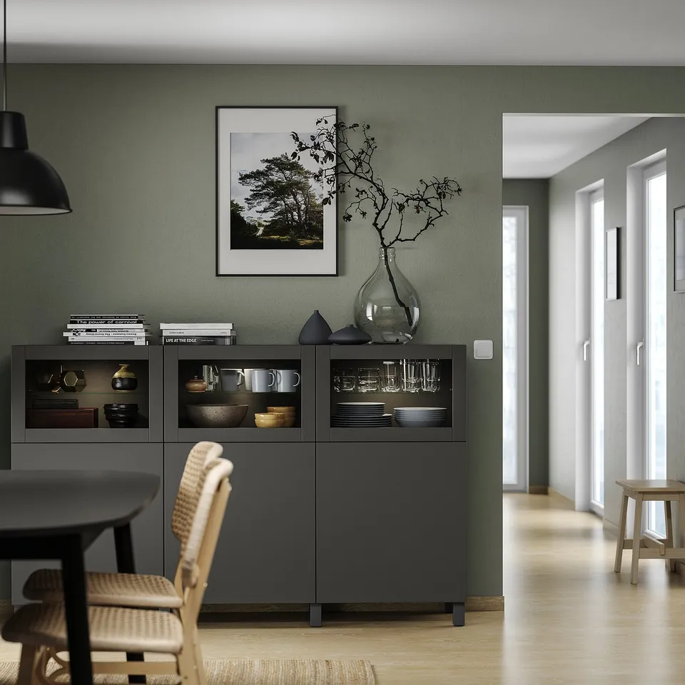 Modern dining room with black BESTÅ unit, sage green walls, wicker chairs, and nature photo.