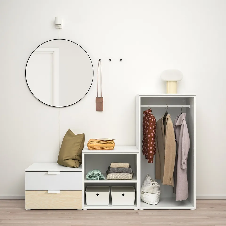 Minimalist closet organiser with hanging coats, folded clothes, and a round wall mirror.