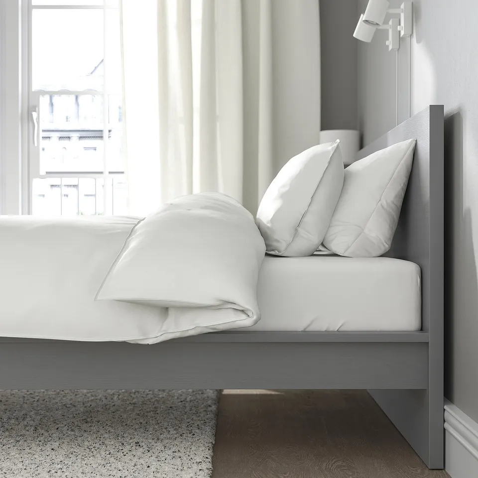 A modern bed with a high headboard and adjustable sides, positioned near a window with sheer curtains, providing a comfortable reading spot.