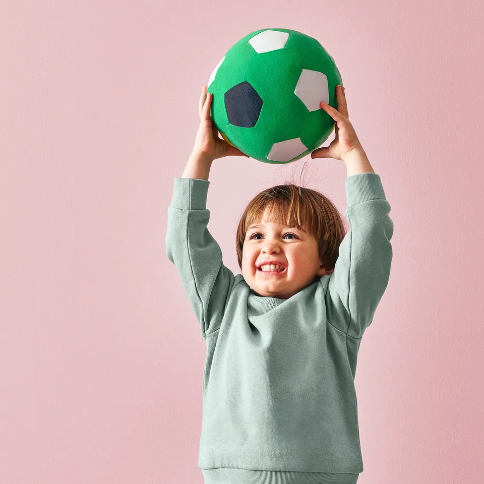 A child holding a green soft football ball above their head, smiling.
