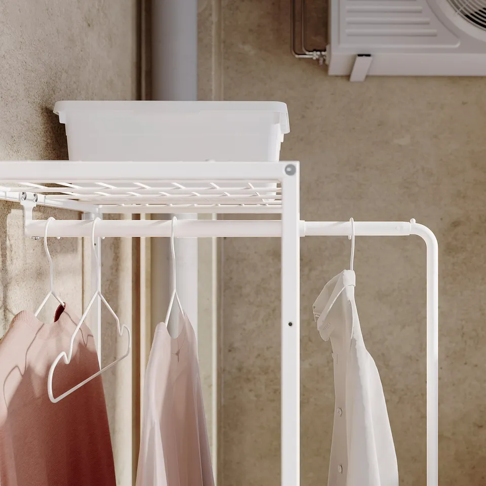 White JOSTEIN storage unit organises laundry with shelving and hangers, hanging pastel clothes.
