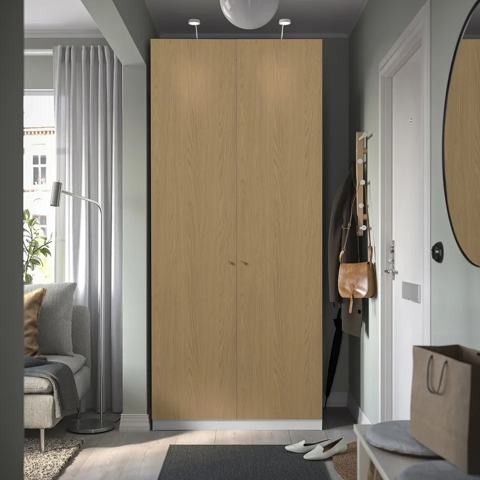 Modern entryway with tall brown PAX wardrobe, coat hooks, and white door.