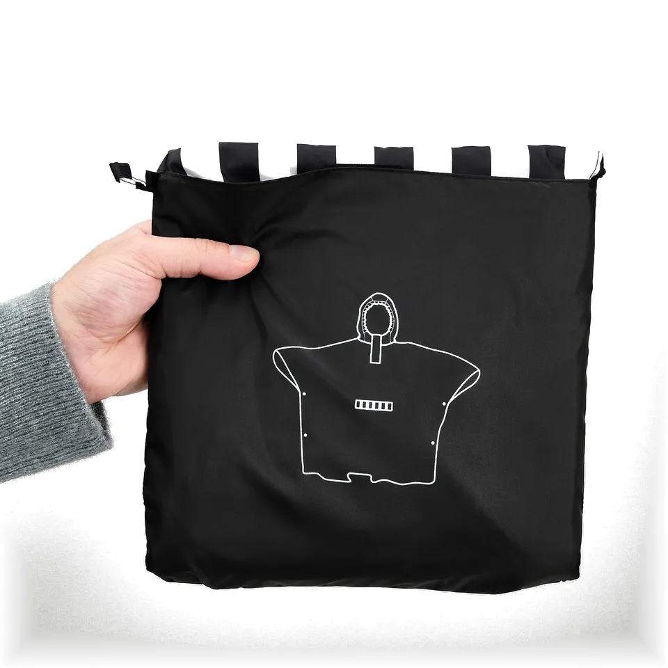 Hand holding black poncho with white stripes at top, featuring a white outline of a shirt with a pocket.