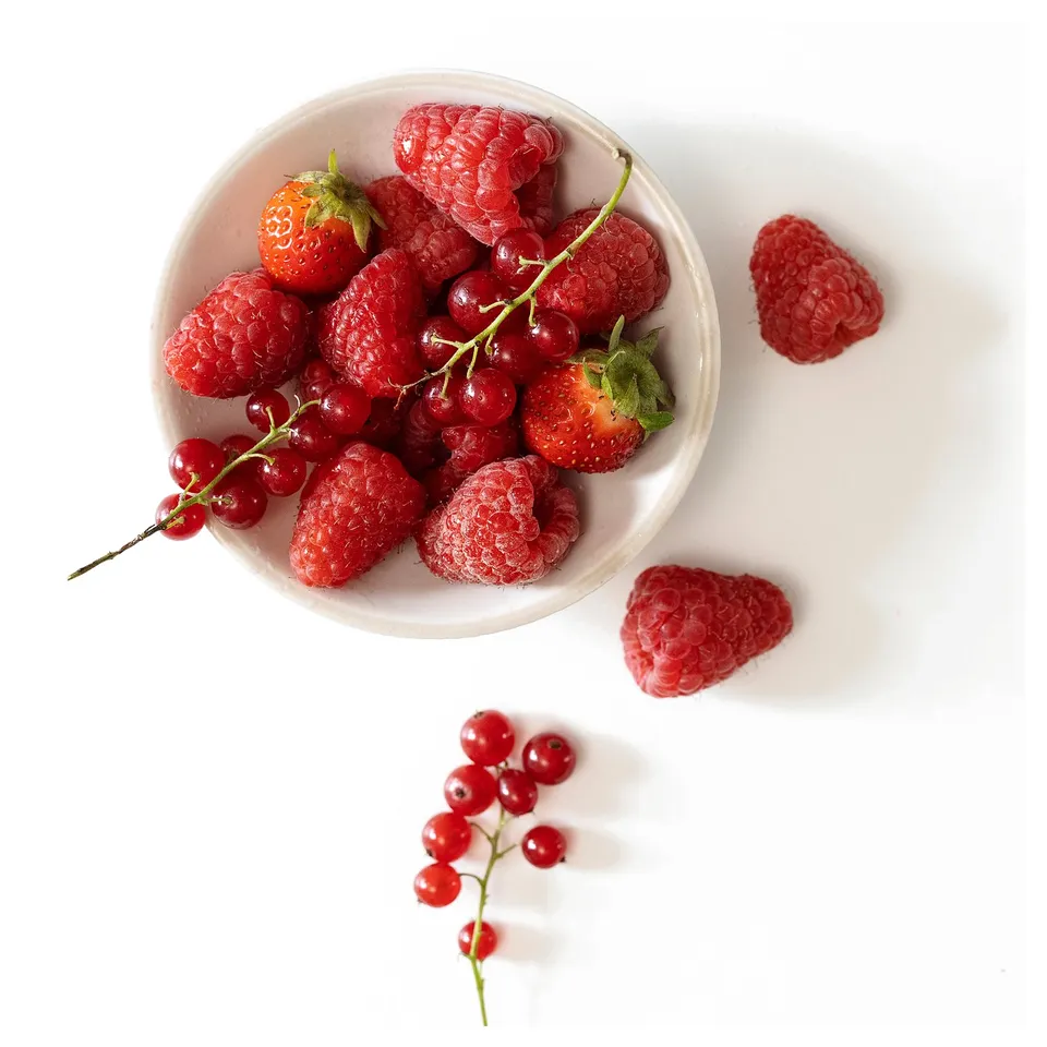 White bowl holds red berries, including strawberries & raspberries. Some scattered. Fresh, simple design.