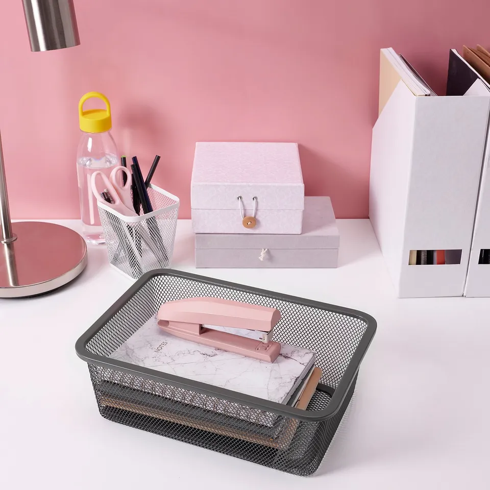 Mesh desk organiser with marble paper, pink scissors, and other office supplies on a pink table.