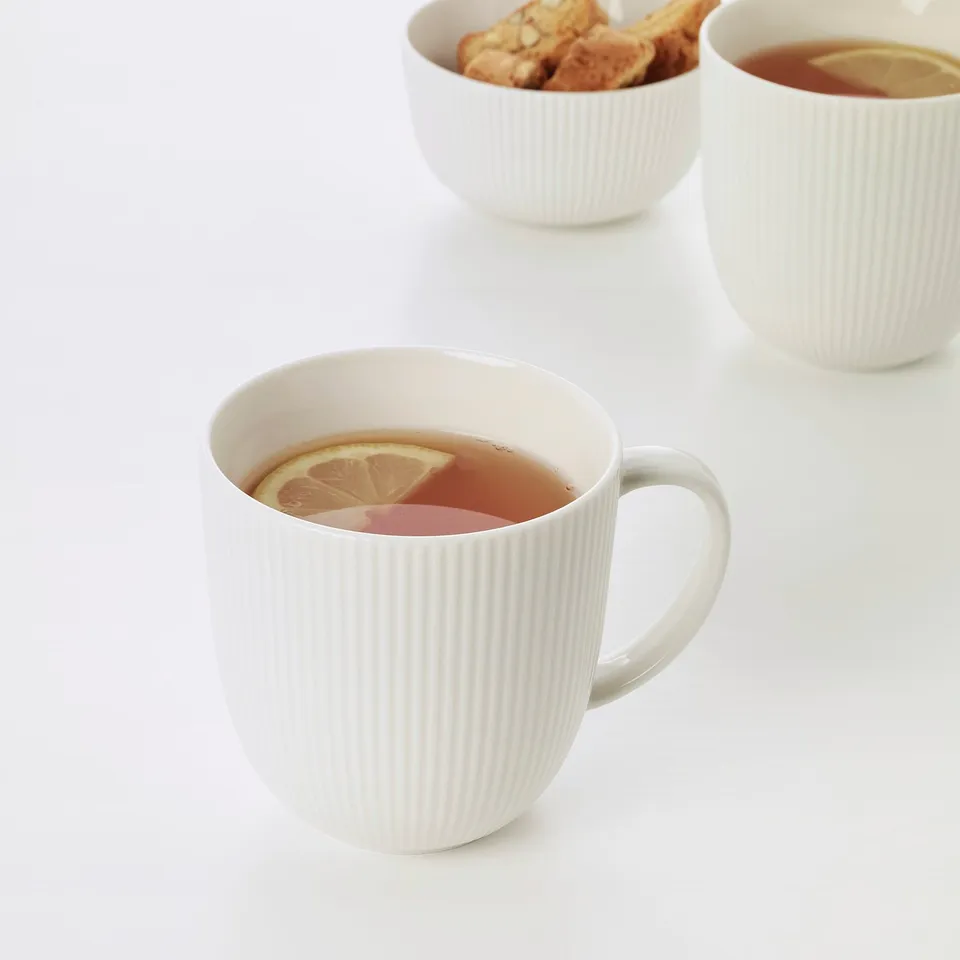 Three white mugs with vertical stripes, containing tea and lemon slices, arranged on a white surface.
