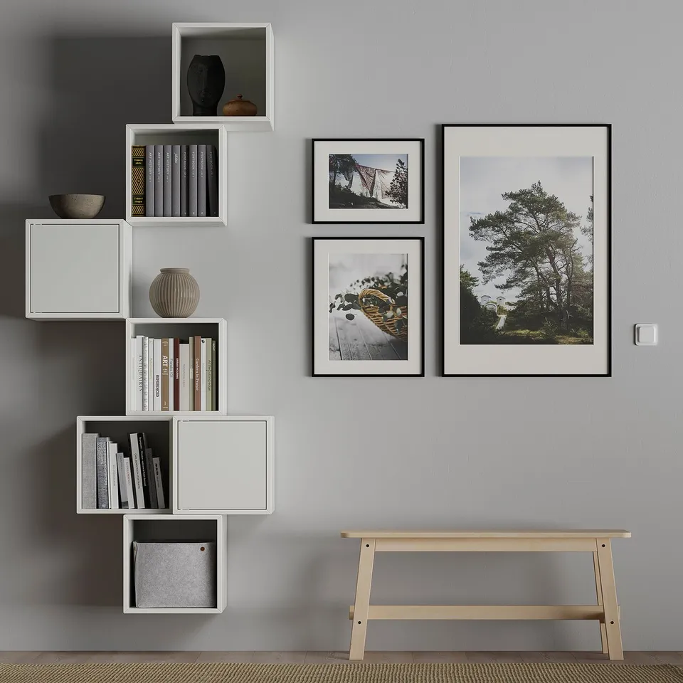 Modern room with grey walls, white modular shelves, and photos. Shelves hold books, a vase, and a basket. Wooden bench below.