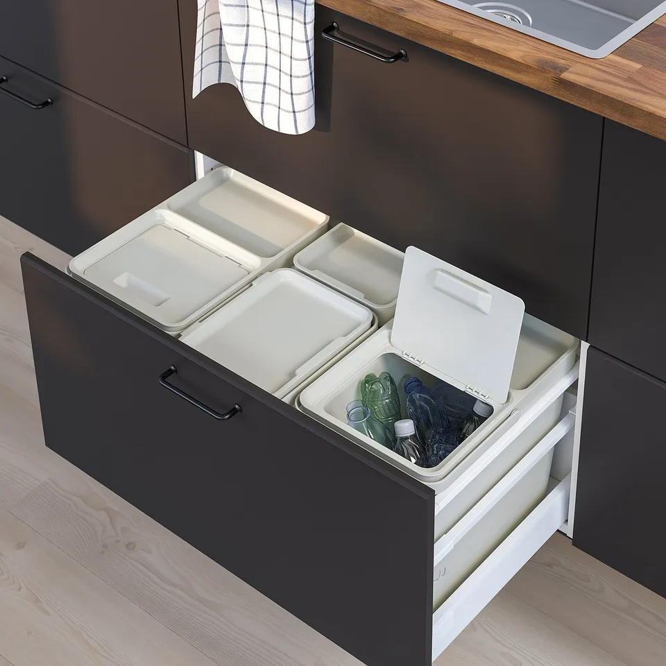 Black kitchen drawer with three white waste sorting bins, each with lids, organised under a wooden countertop.