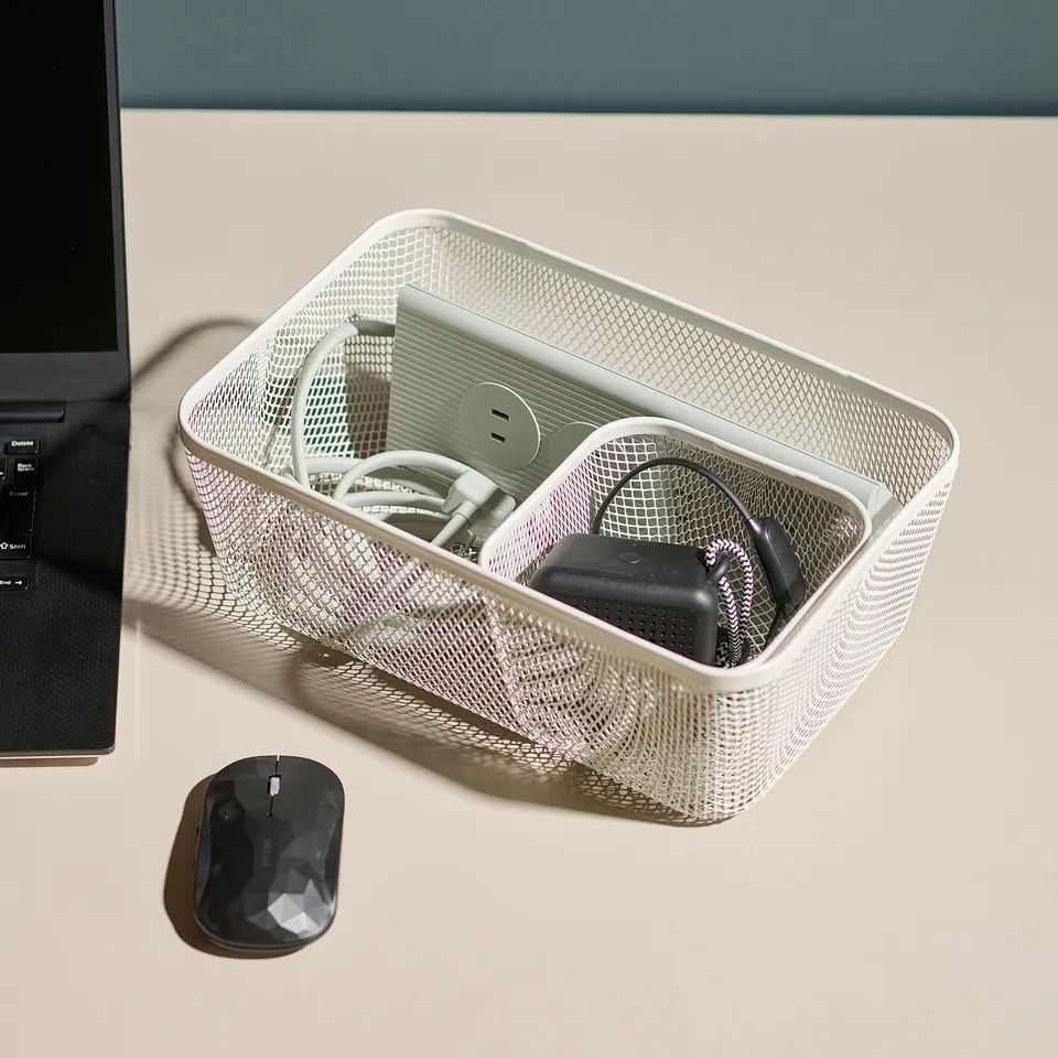 A silver mesh IKEA 365+ basket on a desk organises tech accessories and a charger, demonstrating its versatile storage capabilities beyond food.