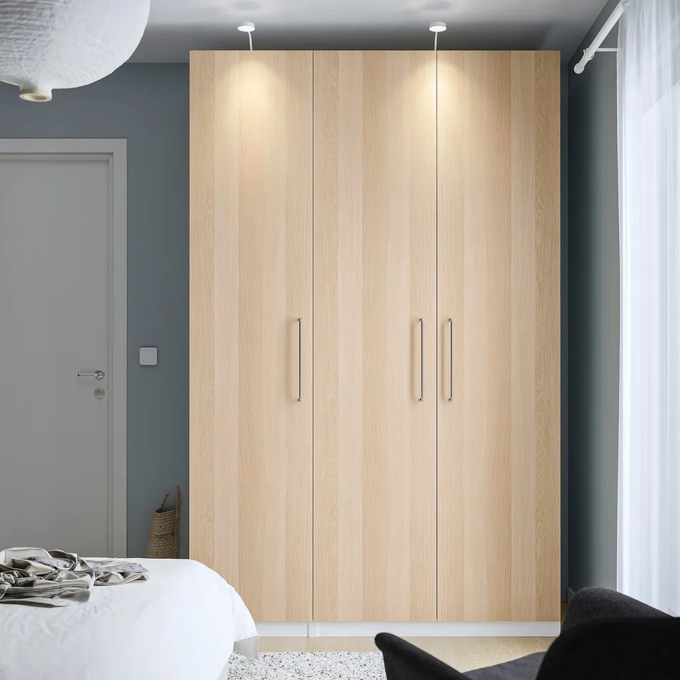 Modern bedroom with tall PAX wardrobe featuring three doors, integrated lighting, and dark grey walls.