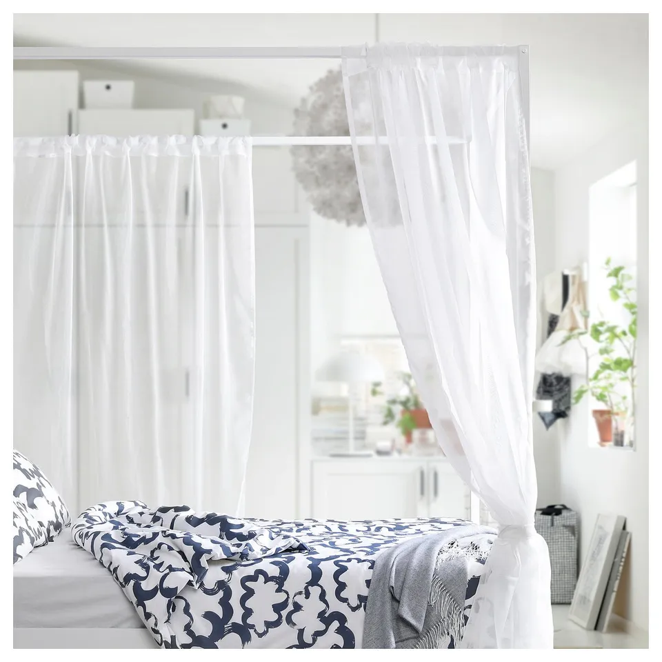 Blue & white bed with metal frame, surrounded by sheer curtains, plants, and baskets.
