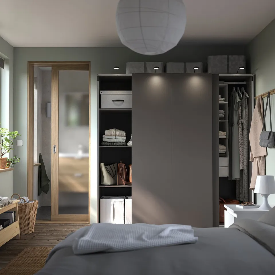 Modern bedroom with black IKEA PAX wardrobe, grey bed, lamp, and wooden door.