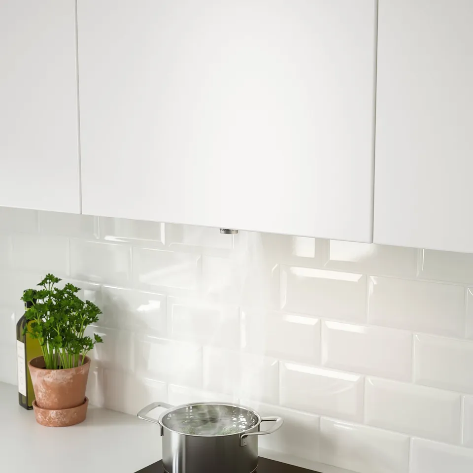 White kitchen with integrated hood. Pots, parsley, and backsplash visible. Extraction system hidden.