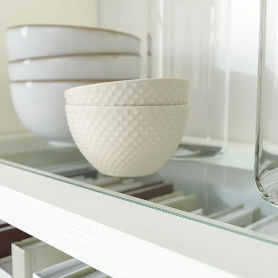 A glass display shelf holds white decorative bowls, stacked plates, and a tall clear glass.