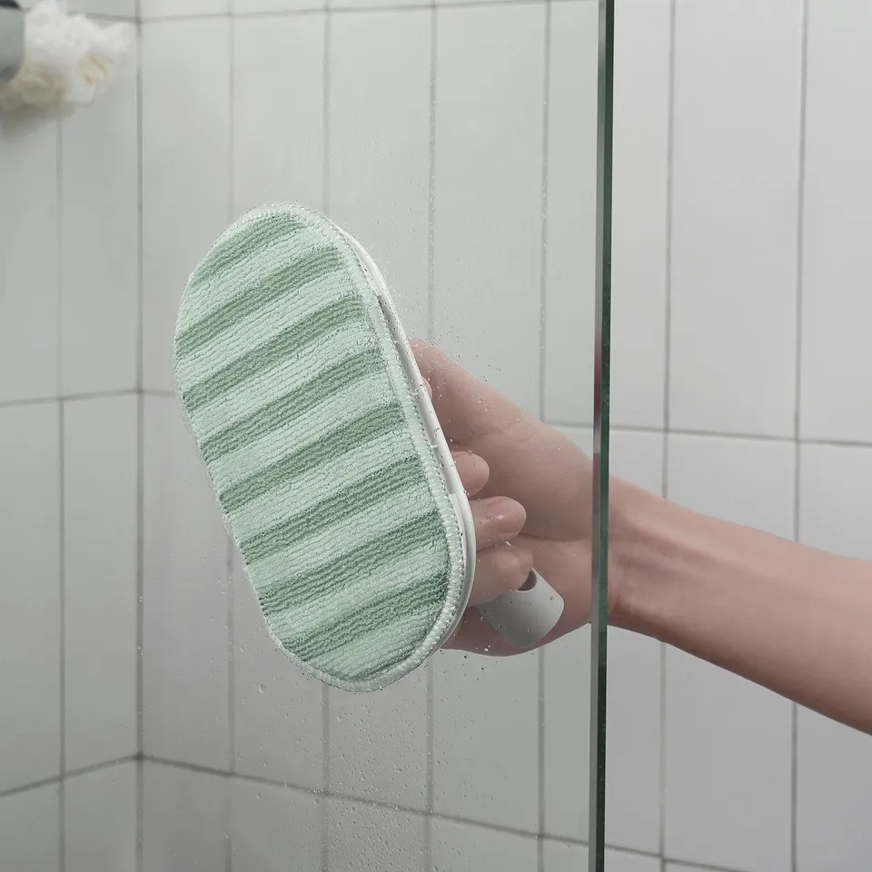 Hand holds a green PEPPRIG microfibre pad against clear glass, ideal for gentle, scratch-free cleaning.