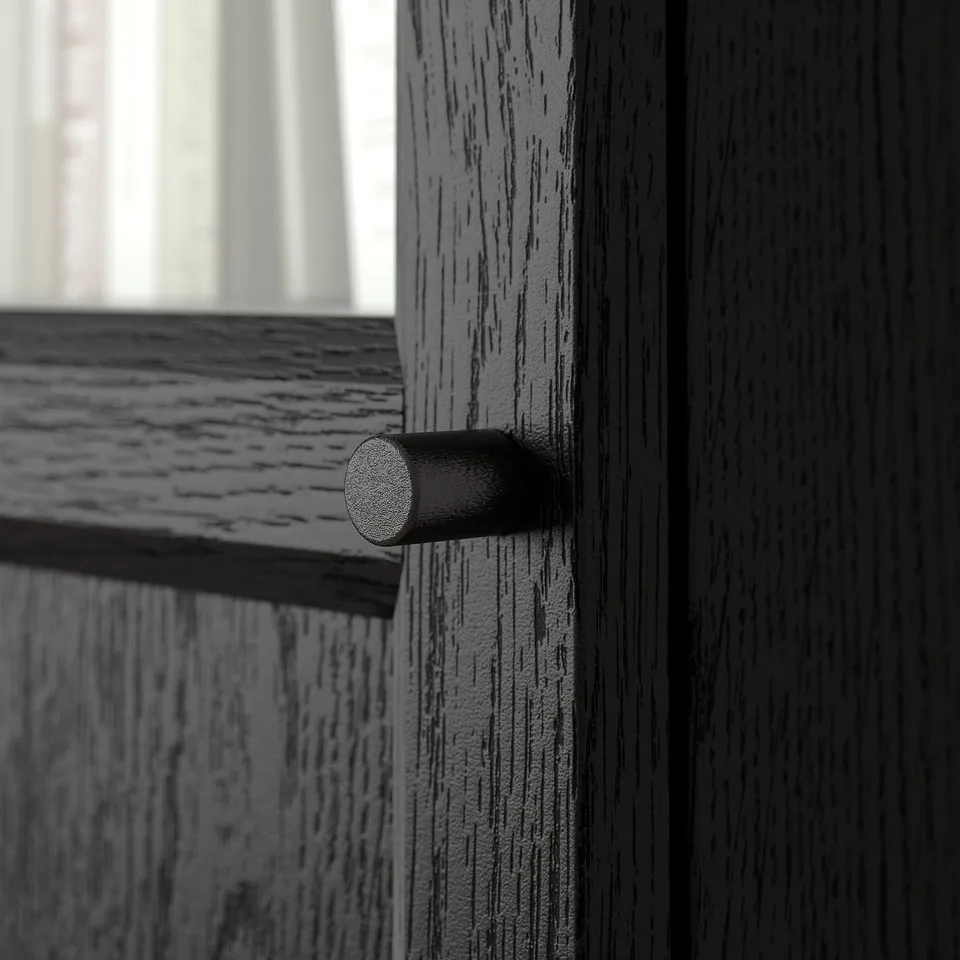 Door hinge detail: close-up view of a round, metallic door hinge on a black wooden structure, showcasing its smooth and polished surface.