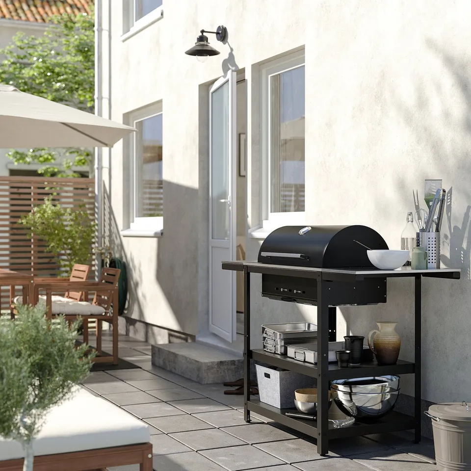 Charcoal grill on patio with table and umbrella.