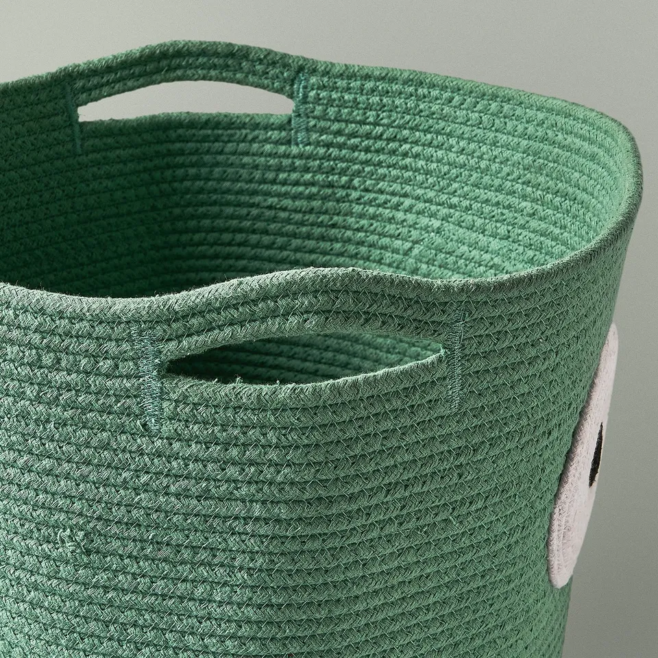 Close-up of a green woven storage basket with large handles, featuring a friendly owl design.