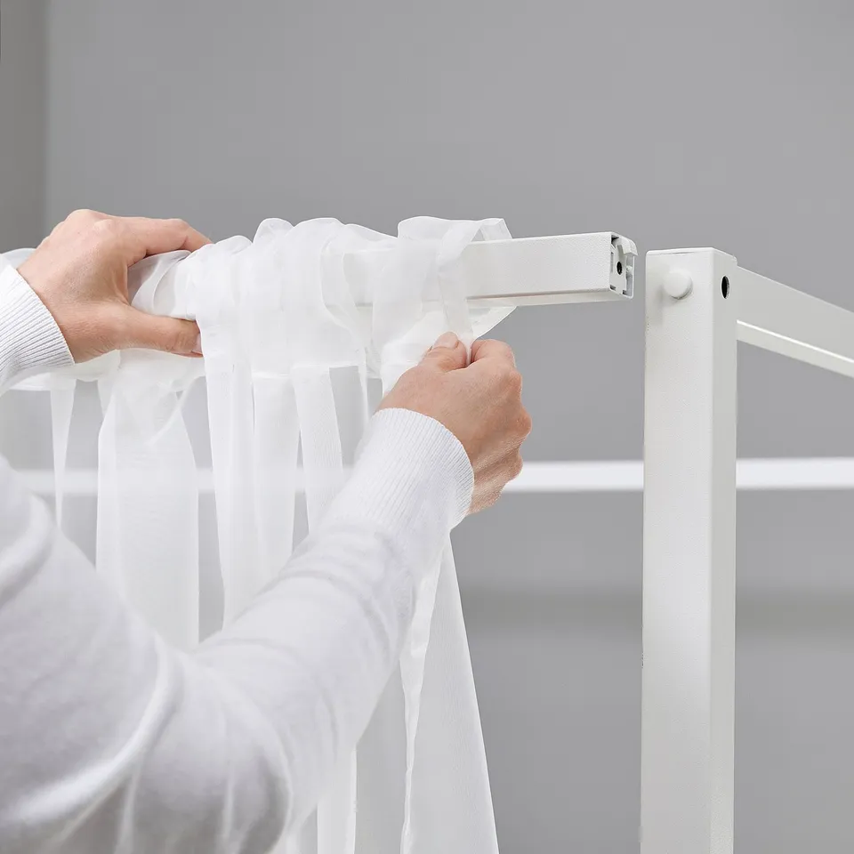 Person adjusting white VITARNA bed frame, showing its sturdy, easy-to-clean design, enhancing home organisation.