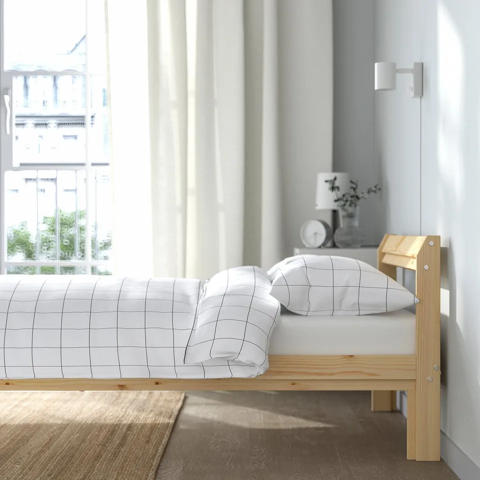 A twin-bed with wooden frame and white grid bedding beside a window.