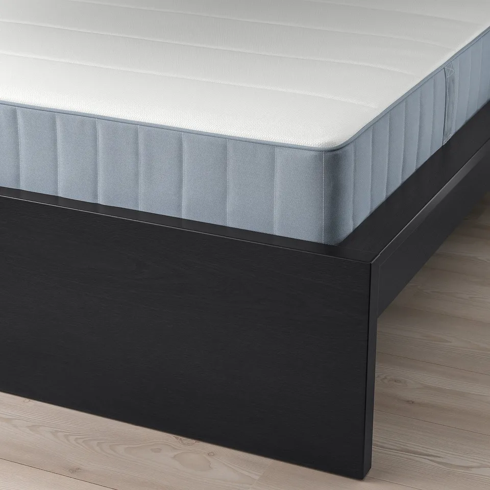 A close-up of a black wooden bed frame with a white quilted mattress, showcasing its sleek design and supportive structure.