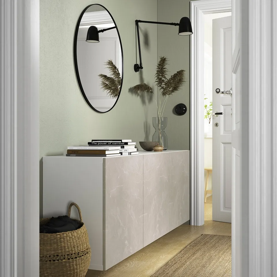 A modern hallway with BESTÅ storage, mirror, books, vase, basket, and lamp, connecting to a bright room with wood floors.