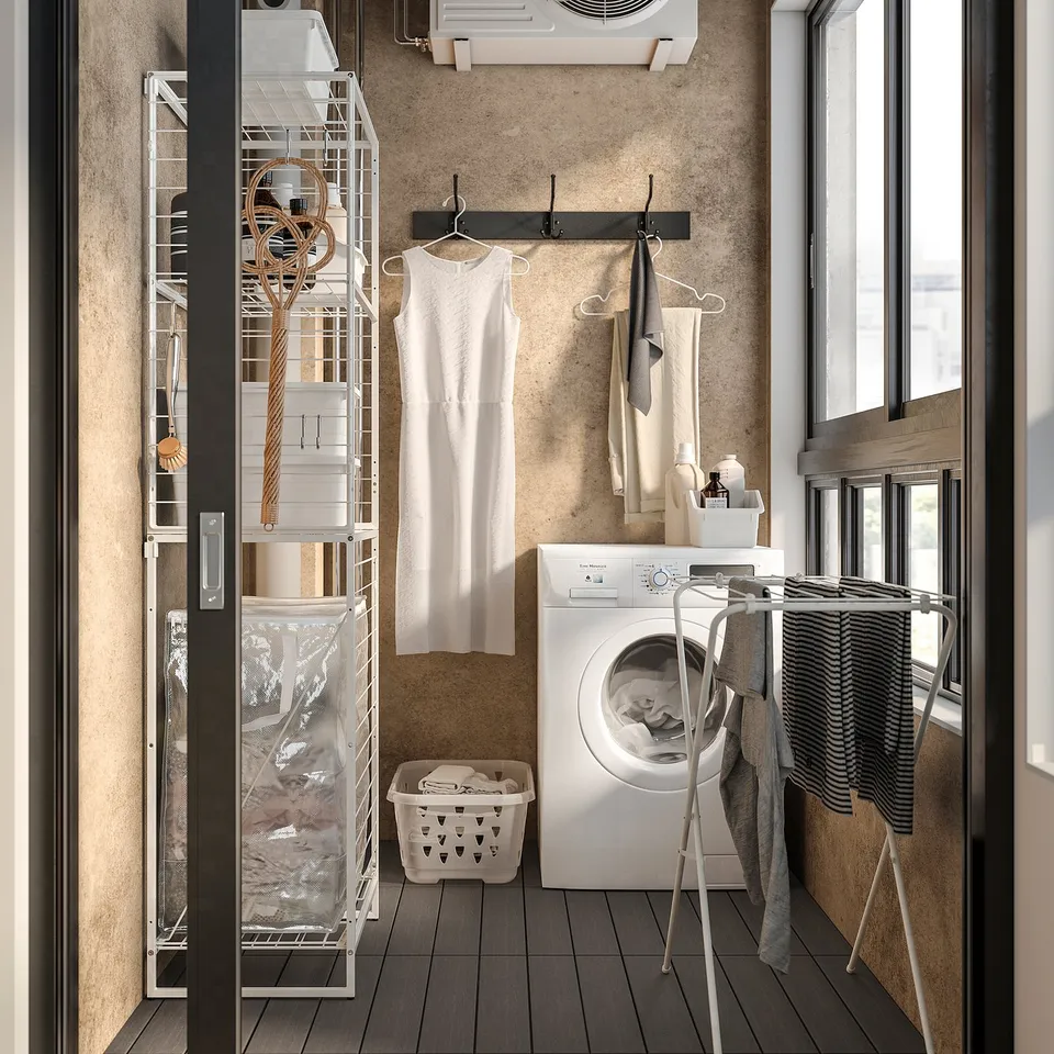 Small, organised laundry room with white JOSTEIN storage shelves. Hanging clothes, washing machine, and drying rack.