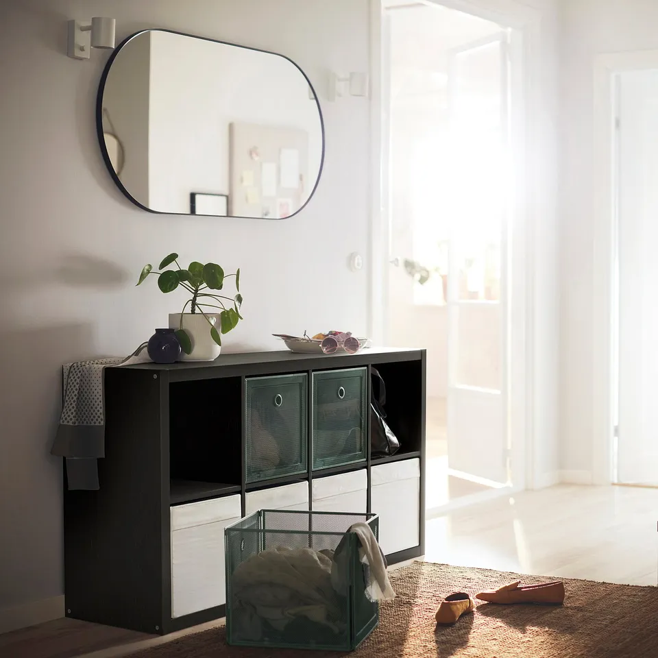 KALLAX black-brown storage unit with mesh drawers and white front, rectangular mirror above, decorative items on top, entryway setting.