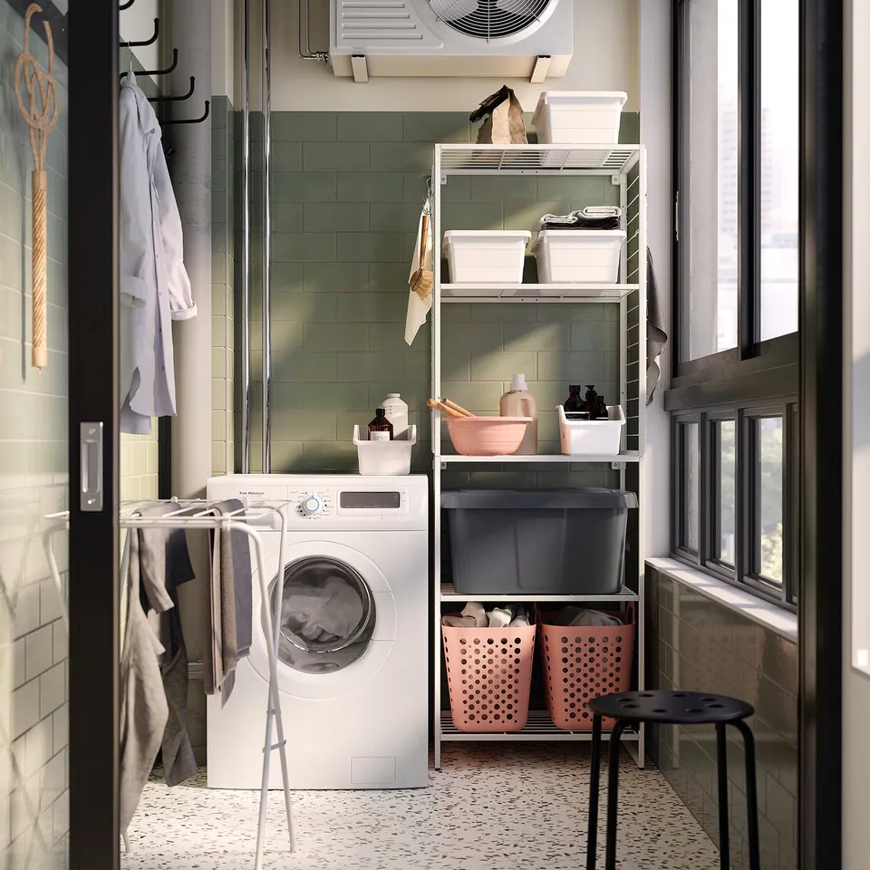 Laundry room with white washer, pink baskets on steel shelves, hanging clothes, tiled walls.