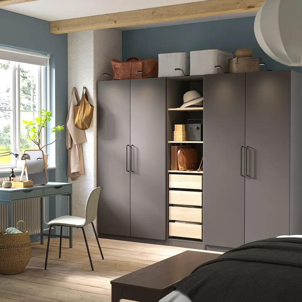 Grey PAX wardrobe with shelves, drawers, and top storage in blue room. Desk, chair, and window with tree view.