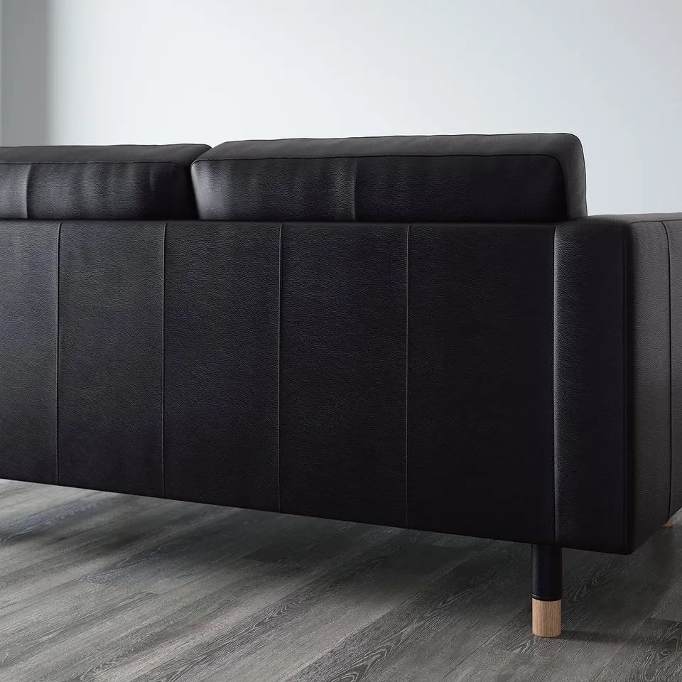 Black leather sectional sofa with wooden legs, showing luxurious seating and backrest detail, set on a wooden floor.