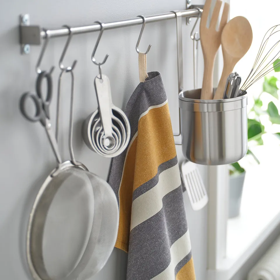 Kitchen rack with tools: strainer, cups, towel, utensils, plant.