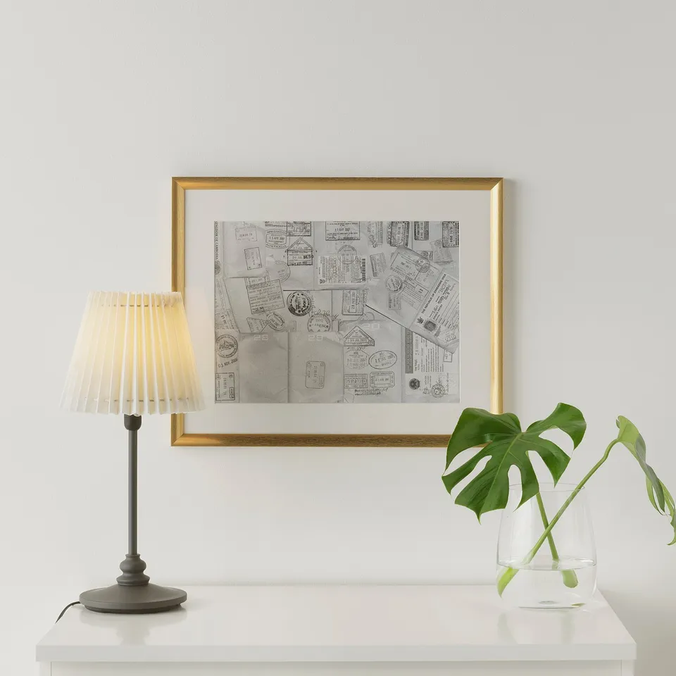 A white console table with a lamp, art frame, and plant.