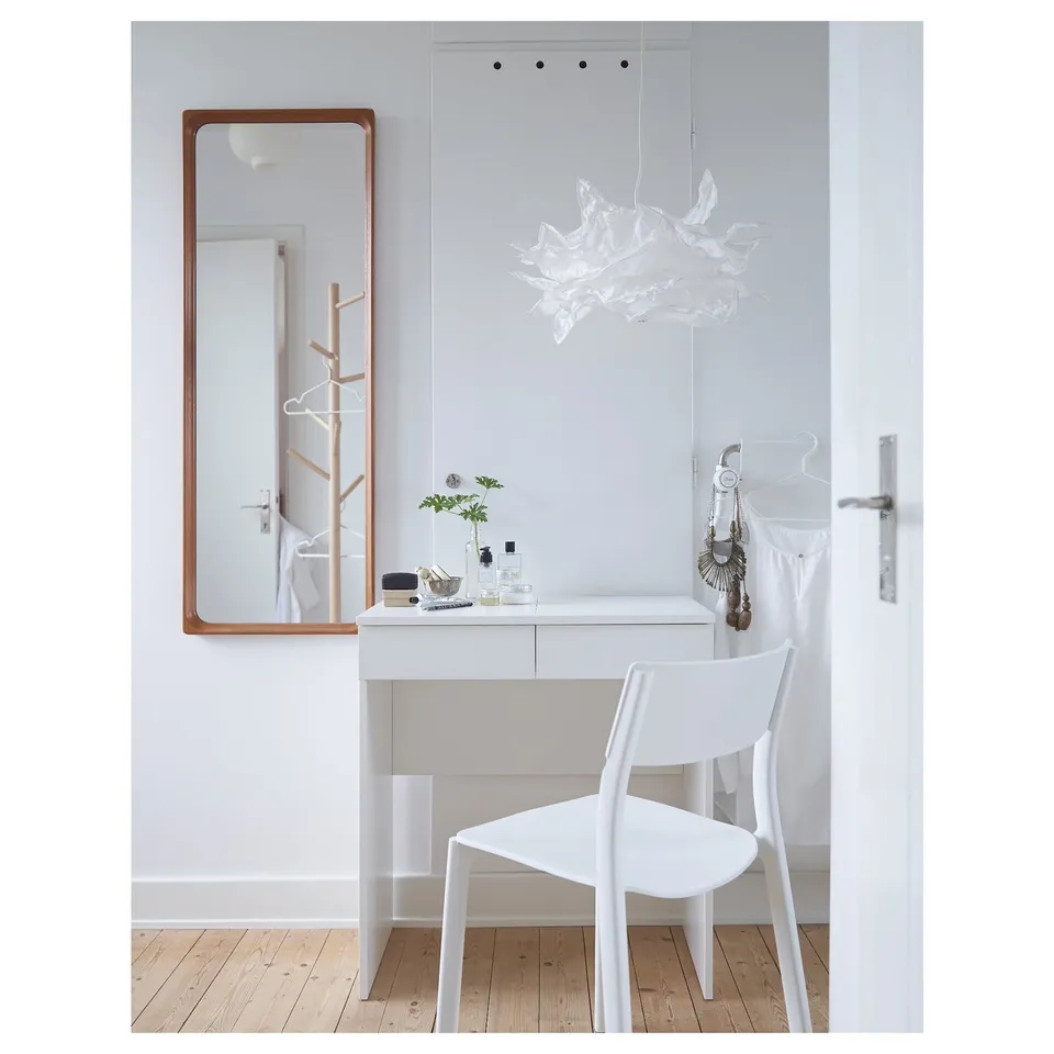 Minimalist dressing table with large mirror, drawers, and white chair. Modern, clean design with vanity items on top.