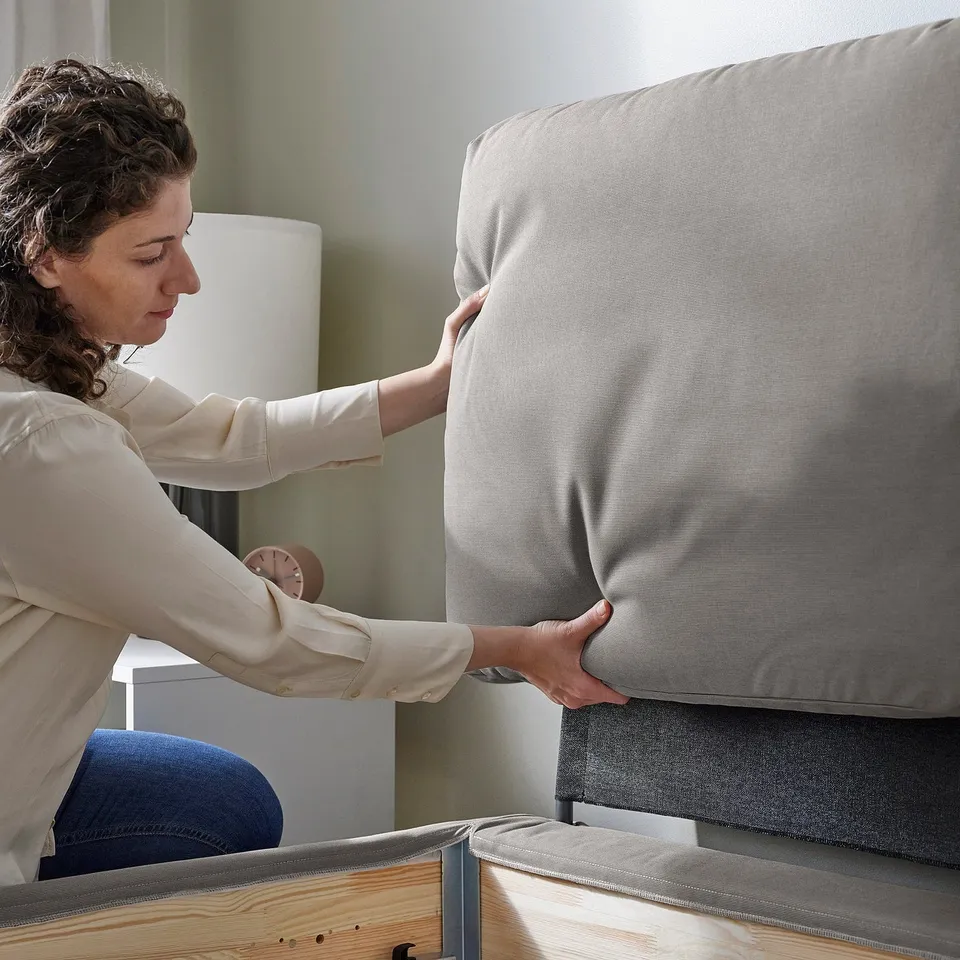 Person adjusting modern bed with washable cover and wooden legs.