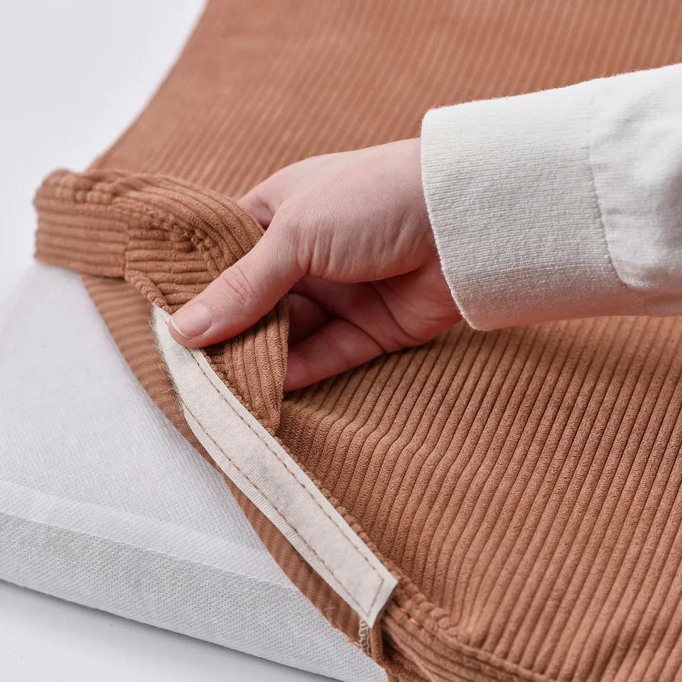 Hand holding brown fabric. Showing removable, washable cover for easy cleaning.