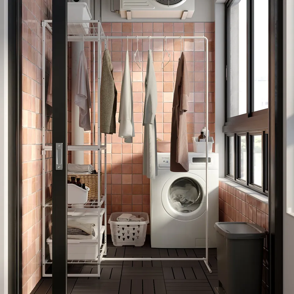 Laundry room with JOSTEIN shelves, drying rack, and washing machine. Beige-tiled walls and dark floor with a window.