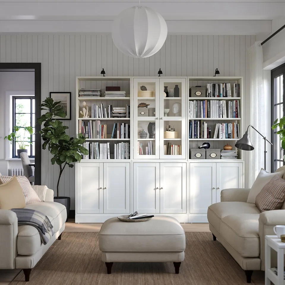 Elegant living room with HAVSTA white pine bookcases, sofa, ottoman, lamp, large window, and plants.