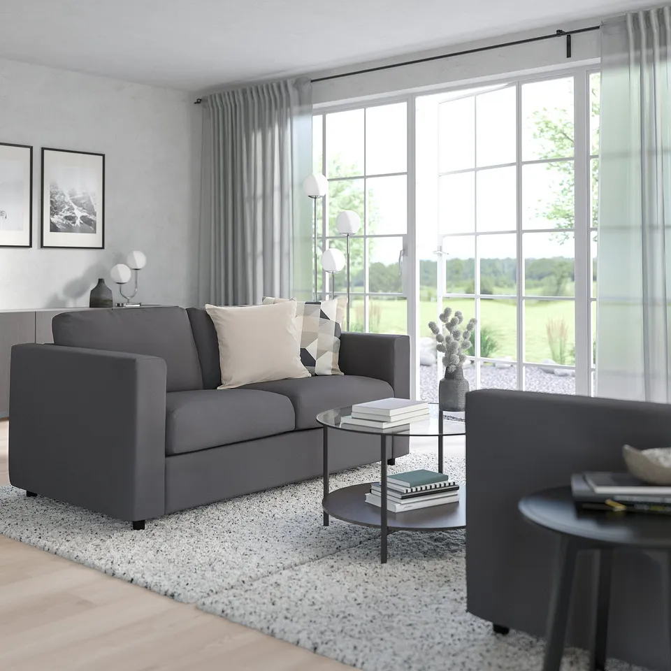 Minimalist living room: grey VIMLE sofa near large window, modern decor, wooden floor, light rug.