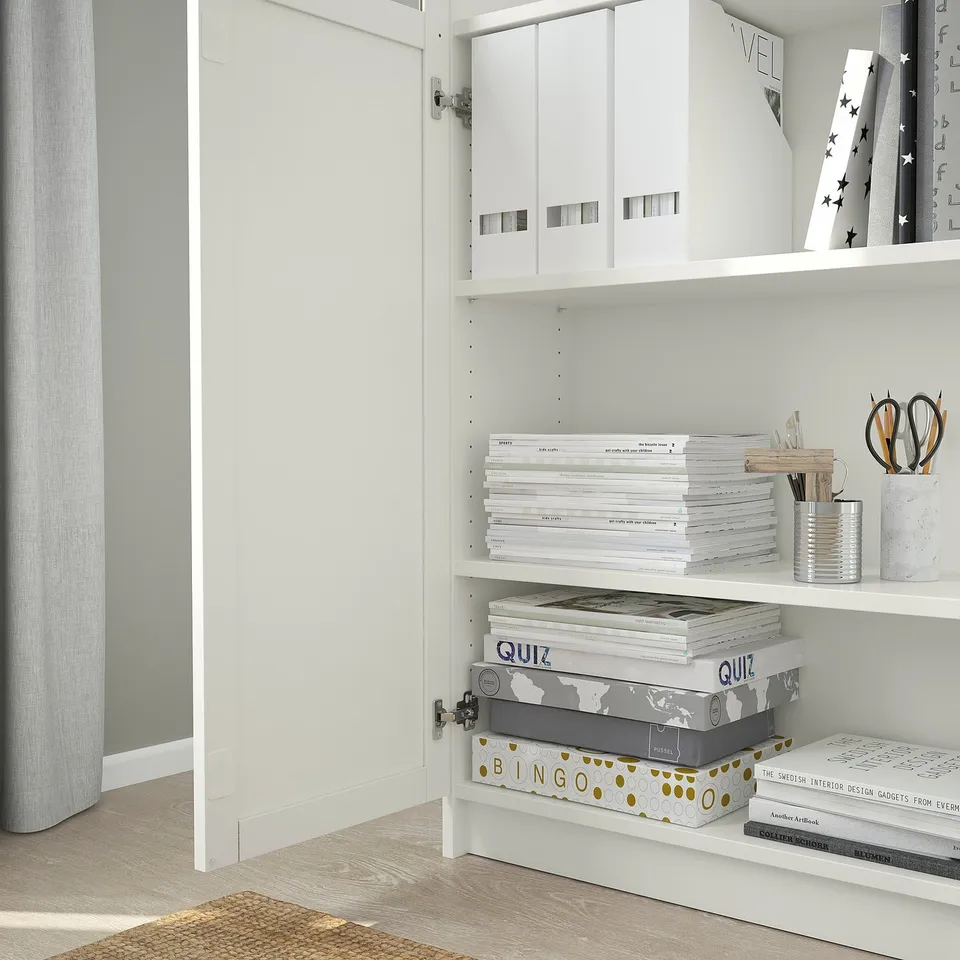 Bookshelf with adjustable shelves, storing white boxes, stacked books, and a canister of writing tools.