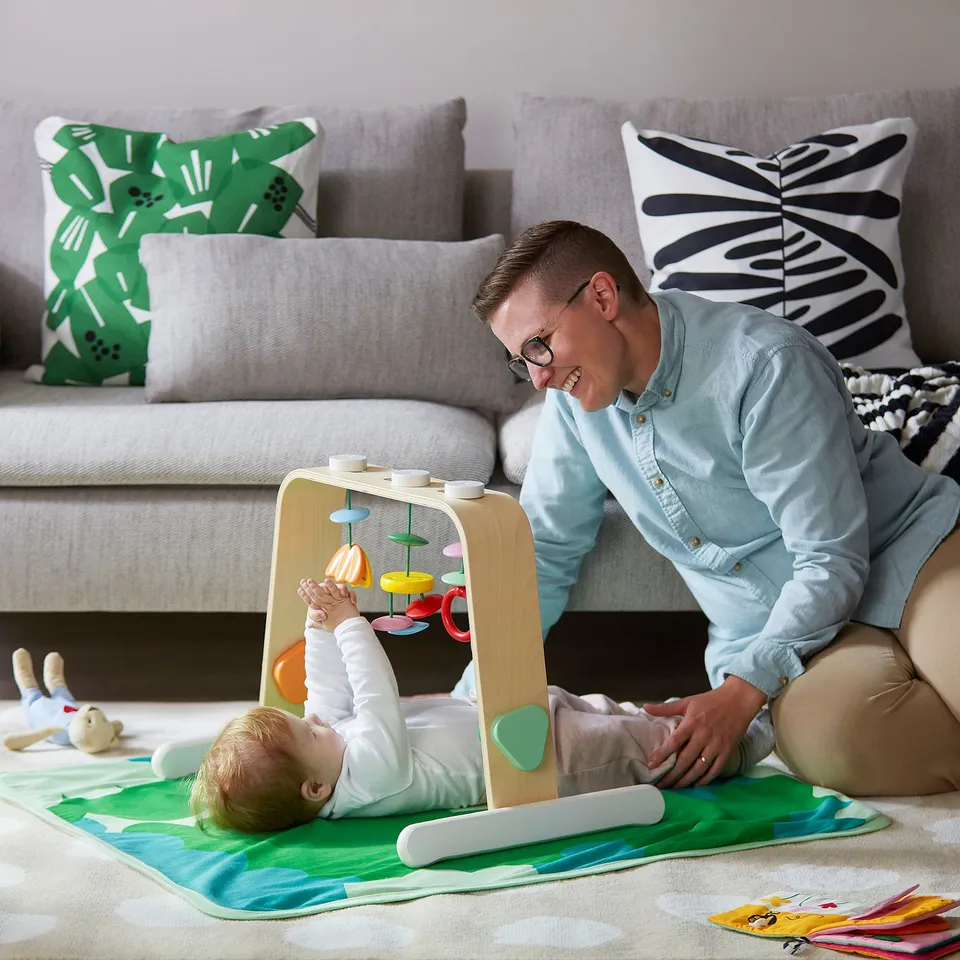 Person plays with baby on colourful gym, promoting hand-eye coordination and sensory development.