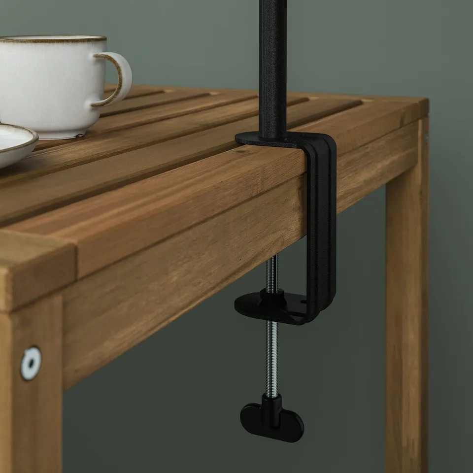 Black clamp holding wooden tables edge, securing rod for hanging decorations.