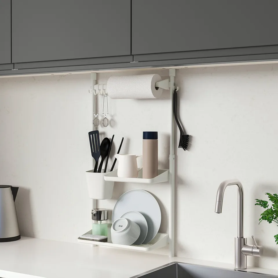 Small white SUNNERSTA wall shelf, holding kitchen items near shiny tap, beneath dark cabinets.
