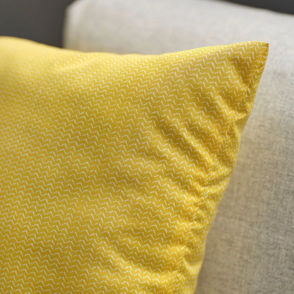 Bright yellow cushion with a subtle pattern and sheen, placed on a light-colored sofa. Feels soft and high-quality.