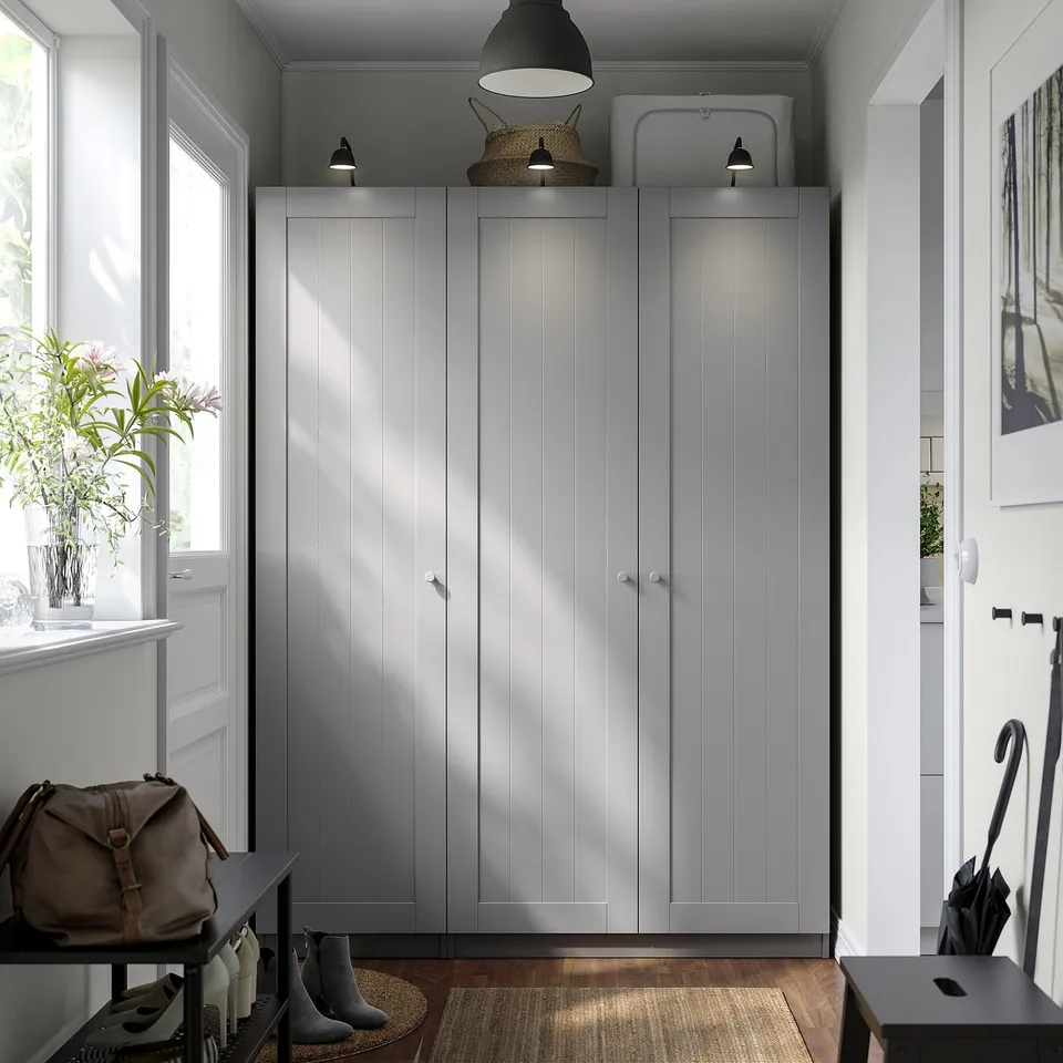 Grey PAX wardrobe with white handles by window, wider than black console table, reflecting clean design.