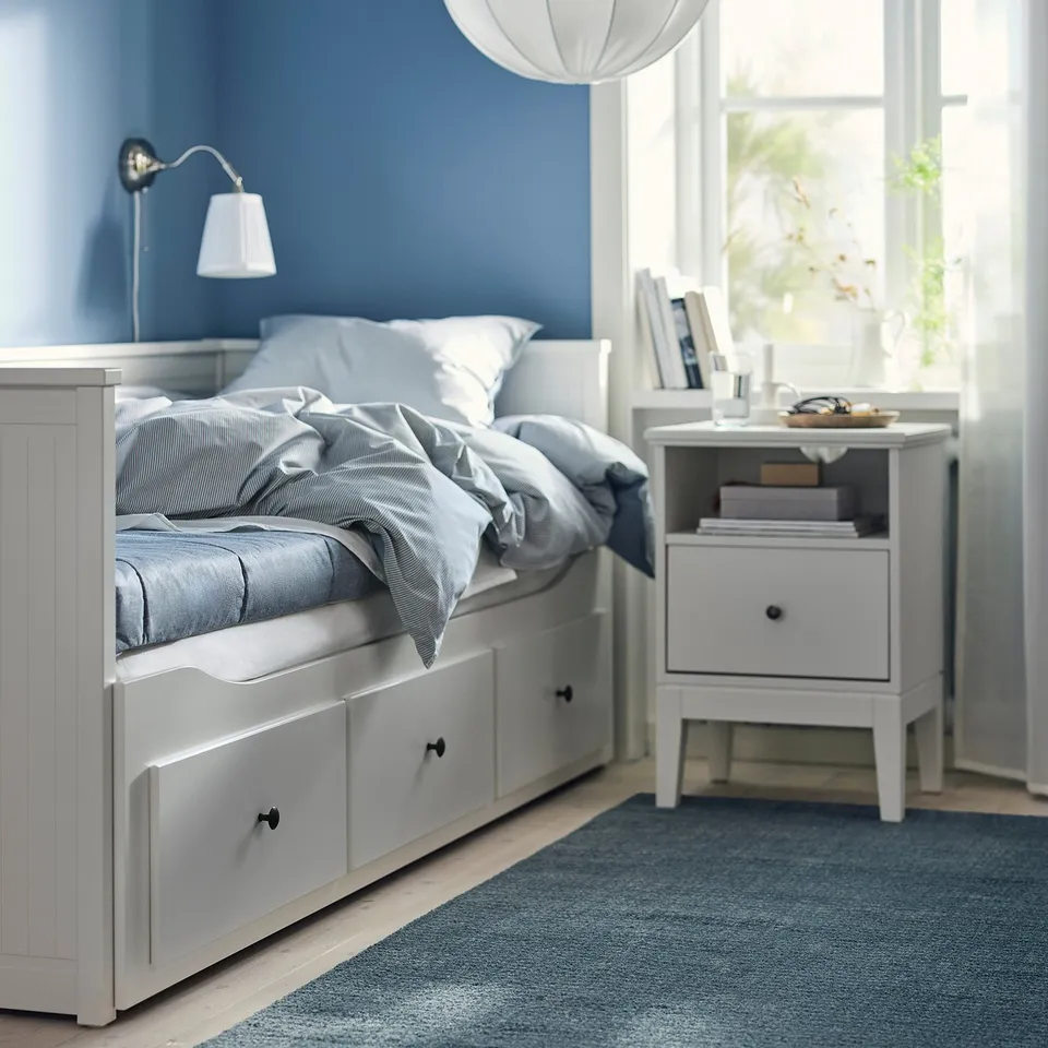 Cosy blue bedroom with white furniture: bed, bedside table, lamps, and large window.