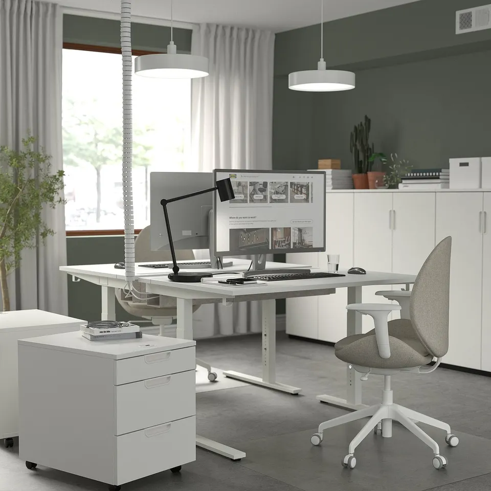 Modern MITTZON standing desk setup with computer, ergonomic chair, and storage in bright room with plants.